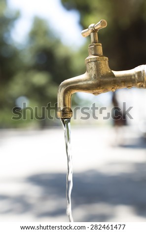 A street tap turned on and releasing water on a sunny day outdoors
