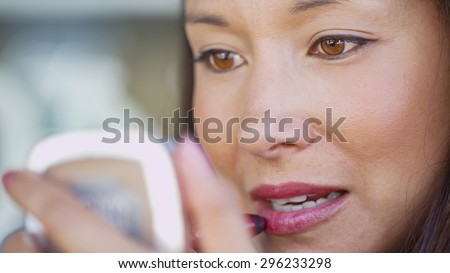 Attractive young woman applying lipstick using a portable vanity mirror