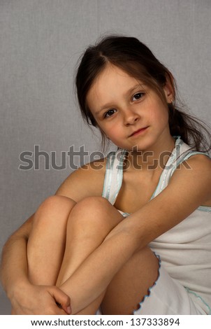 Beautiful  girl hugging his knees, sitting on a gray background
