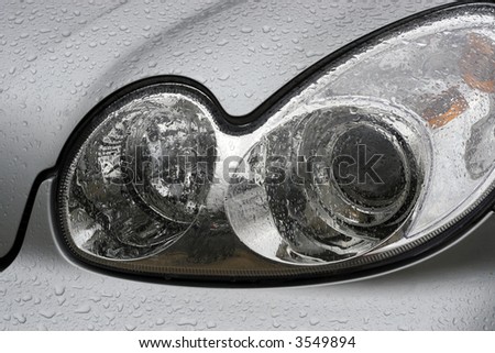 Shiny car with silver paint. Water drops on the hood. Car lamp.