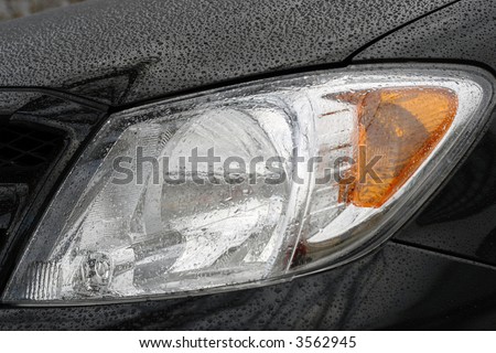 Shiny car with black paint. Water drops on the hood. Car lamp
