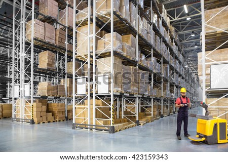 A worker in a huge distribution warehouse with high shelves