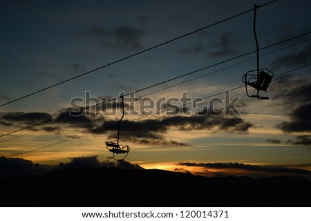 empty ski lift / chairlift silhouette on high mountain over the clouds at sunset