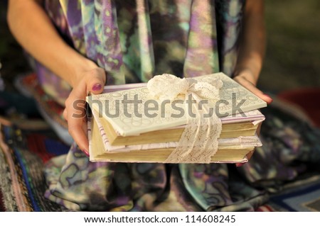 Pile of books in hands. Book with a white envelope tied with lace ribbon