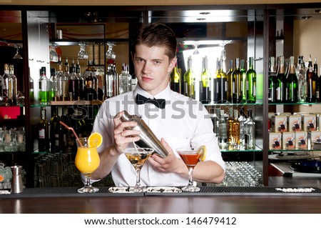Young handsome barman standing in front of the bar and making cocktail drinks.