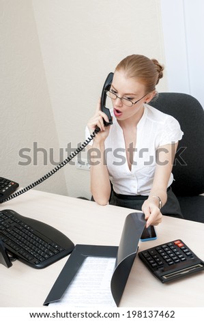 Busy office girl talking on mobile phone and looks into a shocking report.
