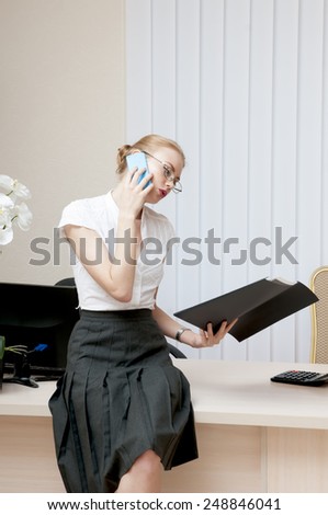 Busy office girl talking on mobile phone and looking at black folder.