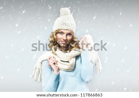 beautiful smiling blonde wearing a blue woolen sweater, a scarf, a knitted cap against snow
