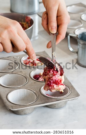 Woman\'s Hands Filling Muffin Tins with Raspberry Muffin Batter Before Baking