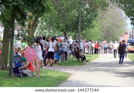 TORONTO - JUNE 23: People lining up in a park in a hot day of Summer on June 23, 2013 in Toronto. Toronto, has a humid continental climate with warm and humid summers.