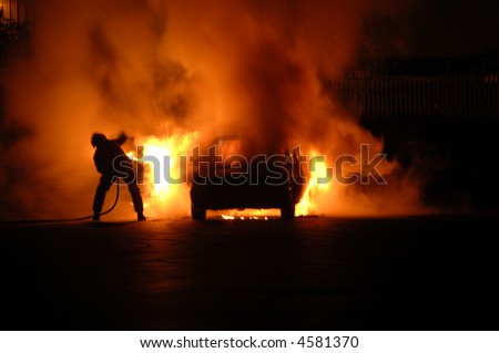 Single fire fighter struggles alone to put out blazing car fire, moving trying to dodge the heat and at the same time aim the hose