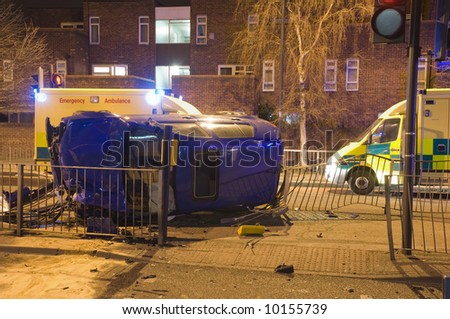 Night time car crash scene showing ambulances in attendance and lit by blue neon lights from surrounding emergency vehicles