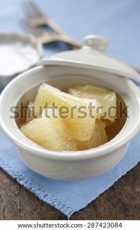 cooked casava or yucca in syrup serve with tiny cup of coconut milk. thai desseert. thai dessert in thai style bowl on cotton blue cloth on old wooden table.