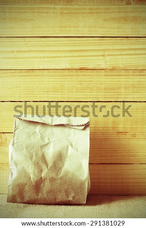 vintage colour style of paper bag of some food in front of wooden background.