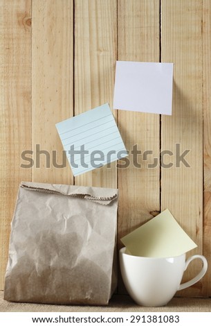 paper bag of some food and coffee cup and note pad paper or note paper on wooden background. breakfast time with planing.