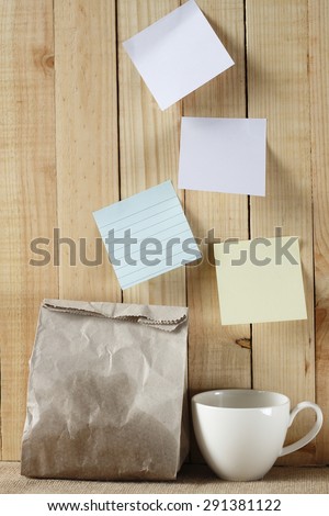 paper bag of some food and coffee cup and note pad paper or note paper on wooden background. breakfast time with planing.