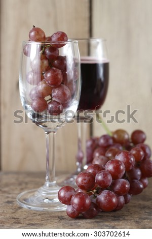 fresh grape in wine glass and glass of red wine on wooden background.