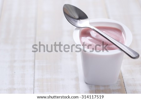 strawberry yogurt in white plastic cup on wooden white background. strawberry yoghurt. pink yogurt.
