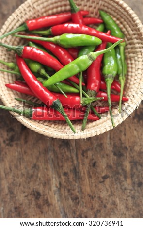 fresh red and green chilli in wicker cup on old wood background. guinea pepper ; bird pepper ; bird-chilli ; small capsicum ; chilli pepper ; tiny fiery chilli ; hot chilli .