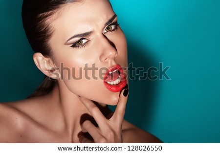 Fashion portrait of beautiful young woman with strong face expression. Touching her chin with hand. Black nails manicure fashion makeup long black eyelashes red lipstick. Blue shaded background.