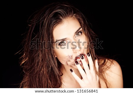 Fashion portrait of beautiful young woman smudging her black lipstick. Powerful face expression, blown hairstyle. Strong makeup long black eyelashes dark lipstick. Black background.
