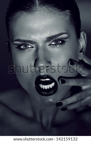 Fashion portrait of beautiful young woman with strong face expression. Touching her face with hand. Black nails manicure fashion makeup long black eyelashes dark lipstick. Monochrome colors.