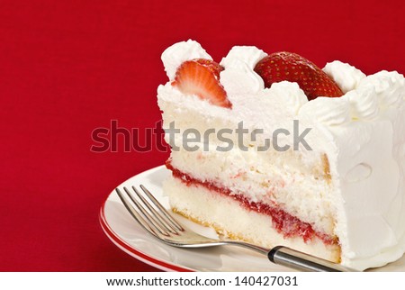 Slice of homemade strawberry cream cake against red background