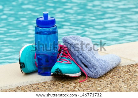 Blue Water Bottle With Running Shoes And Towel By Pool. Exercise And Hydration Concept. Copy Space.