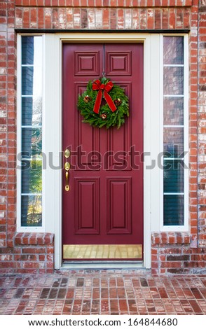Christmas wreath hanging on a red wooden door of a brick house