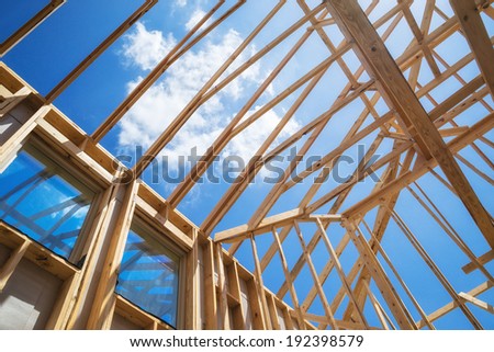 New construction home framing against blue sky, closeup of ceiling frame.
