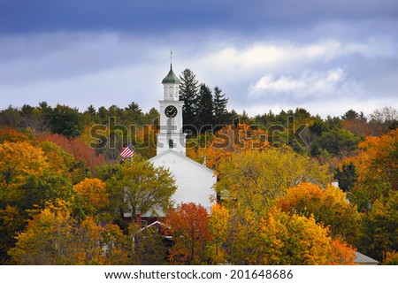 White country church and American flag surrounded by autumn colors in New England