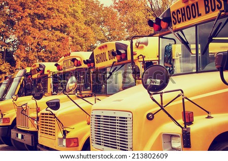 Row of yellow school buses against autumn trees. Shallow depth of field, vintage filter effects.