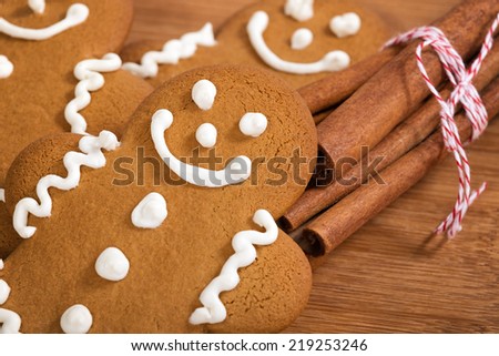 Freshly baked gingerbread man cookies with cinnamon sticks on wooden cutting board, closeup