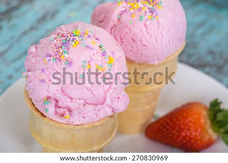 Strawberry ice cream with sprinkles in waffle cups against wooden vintage background, top view