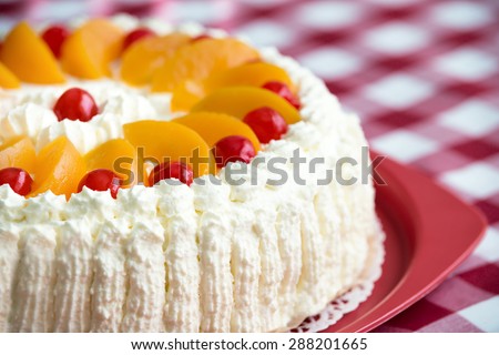 Homemade cream cake with peaches and cherries, closeup with shallow depth of field