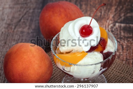 Vanilla peach melba ice cream with whipped cream and a cherry, wooden dark vintage background