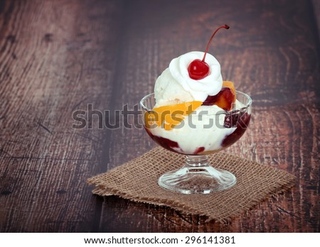 Vanilla peach melba ice cream with whipped cream and a cherry, wooden dark vintage background