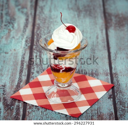 Vanilla peach melba ice cream with whipped cream and a cherry on wooden vintage background