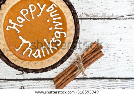 Pumpkin pie with Happy Thanksgiving text. Displayed on vintage wooden table with cinnamon sticks. Top view.
