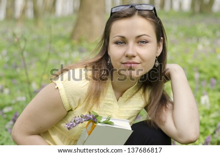 Portrait of beautiful smiling girl with book and glasses in spring forest