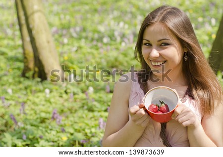 smiling beautiful girl is holding red cup with strawberries