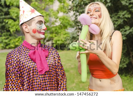 Portrait of a smiling man dressed like a clown trying to present a balloon to a happy girl with butterfly makeup