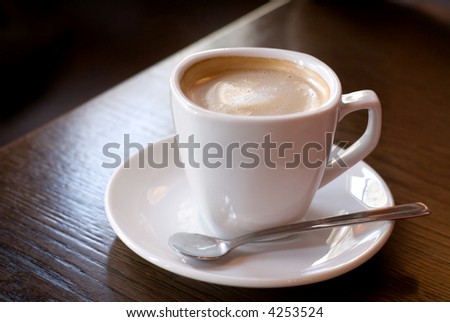 Cup of coffee (focus on the froth surface) on the cafe table. Shallow depth of field.