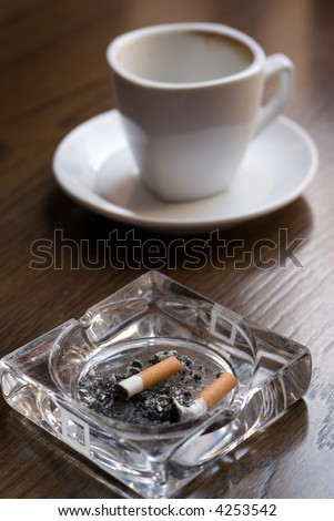 Ashtray and empty coffee cup on the cafe table. Shallow depth of field (focus on the cigarette butt).
