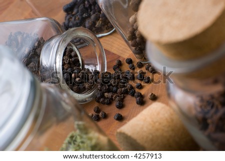 Spilled black pepper seeds from glass jar onto cutting board among other condiments - allspice,juniper etc.