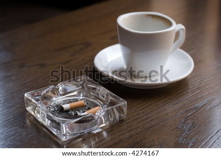 Ashtray and empty coffe cup on the cafe table. Shallow depth of field (focus on the cigarette butt).