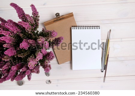 Open white and kraft notepads on the wooden table. Brush and flower. Mock up on the wood.