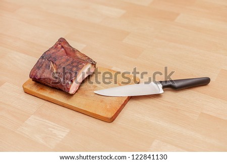 Homemade smoked meat on wooden cutting board with big knife