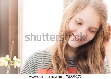Nature portrait of young smiling blonde christian girl before windows with sunshine backlight