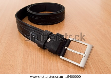 black leather belt with chrome-finished buckle on wood table